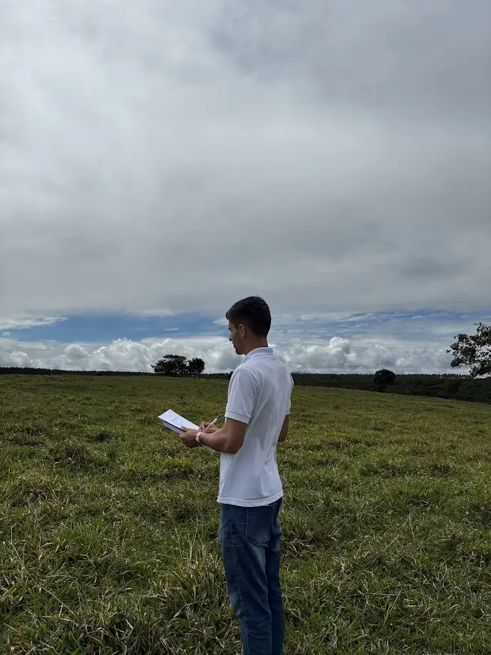 Ralph Araujo fazendo anotações em uma prancheta durante vistoria de imóvel rural, em área de pastagem