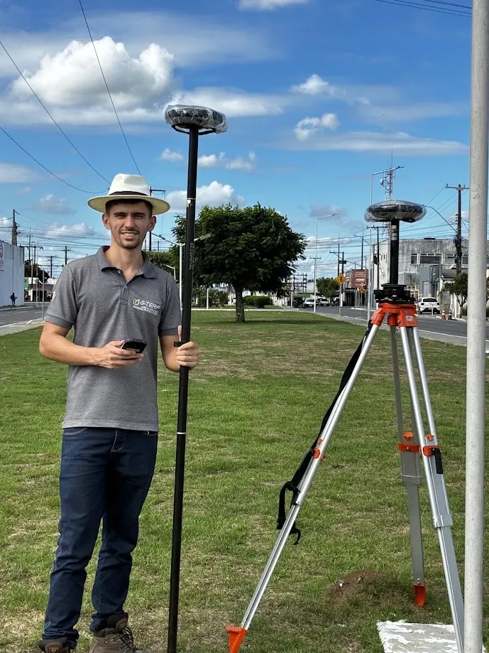 Ralph Araujo segurando bastão com receptor GNSS e coletora, ao lado de um segundo receptor montado em tripé