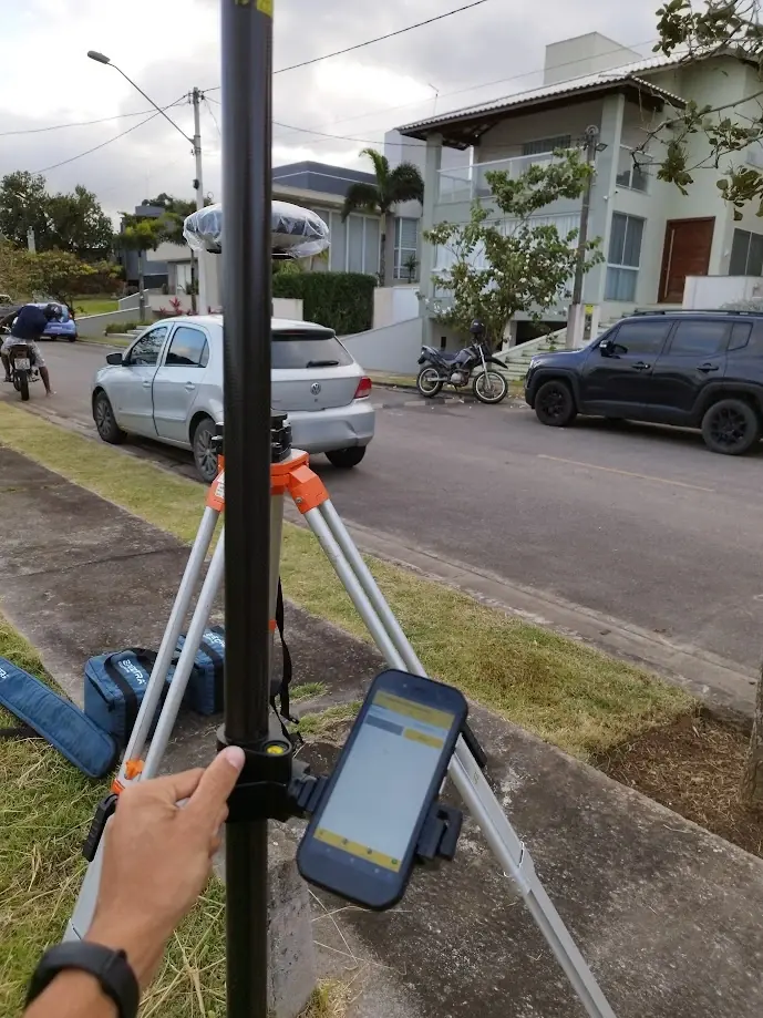 Bastão com coletora e receptor base em tripé numa calçada gramada de via residencial, com casas ao fundo